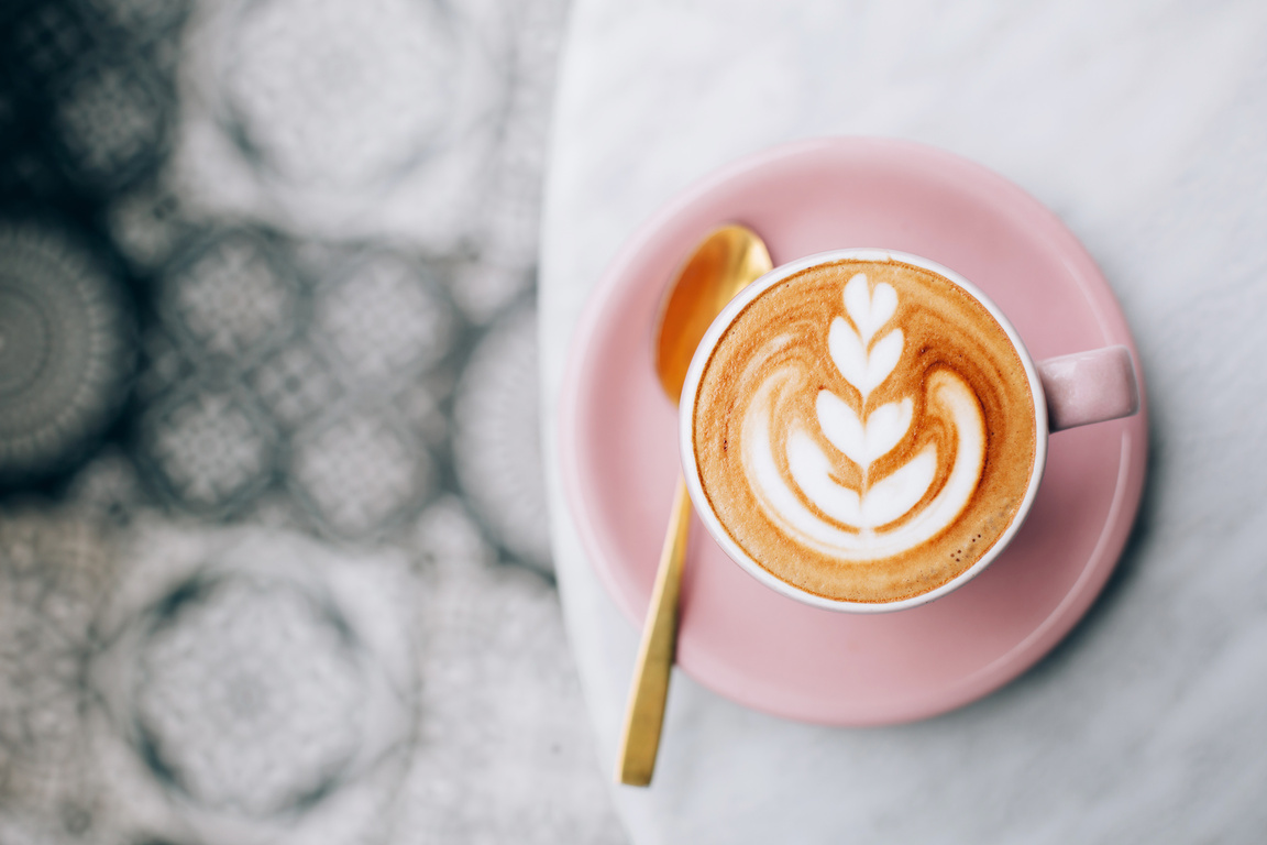a cup of cappuccino sits on a pink plate with a gold spoon