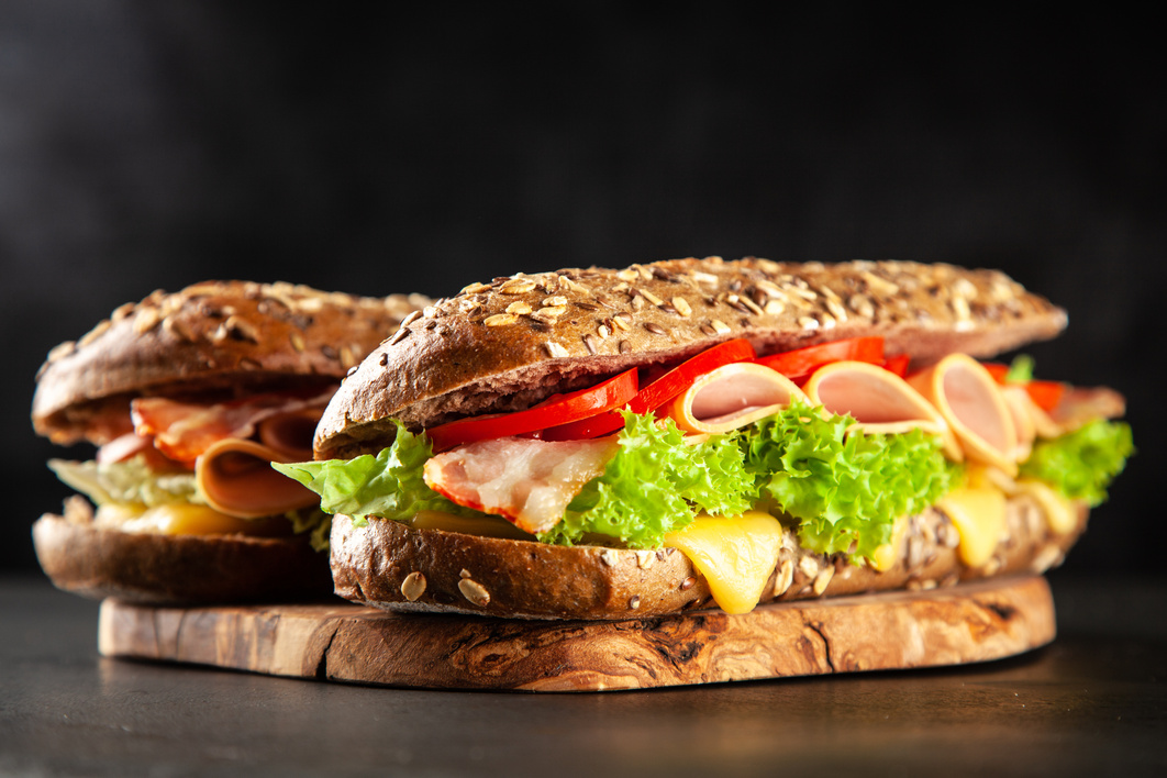 sandwich with ham, cheese, lettuce and tomato on a wooden cutting board