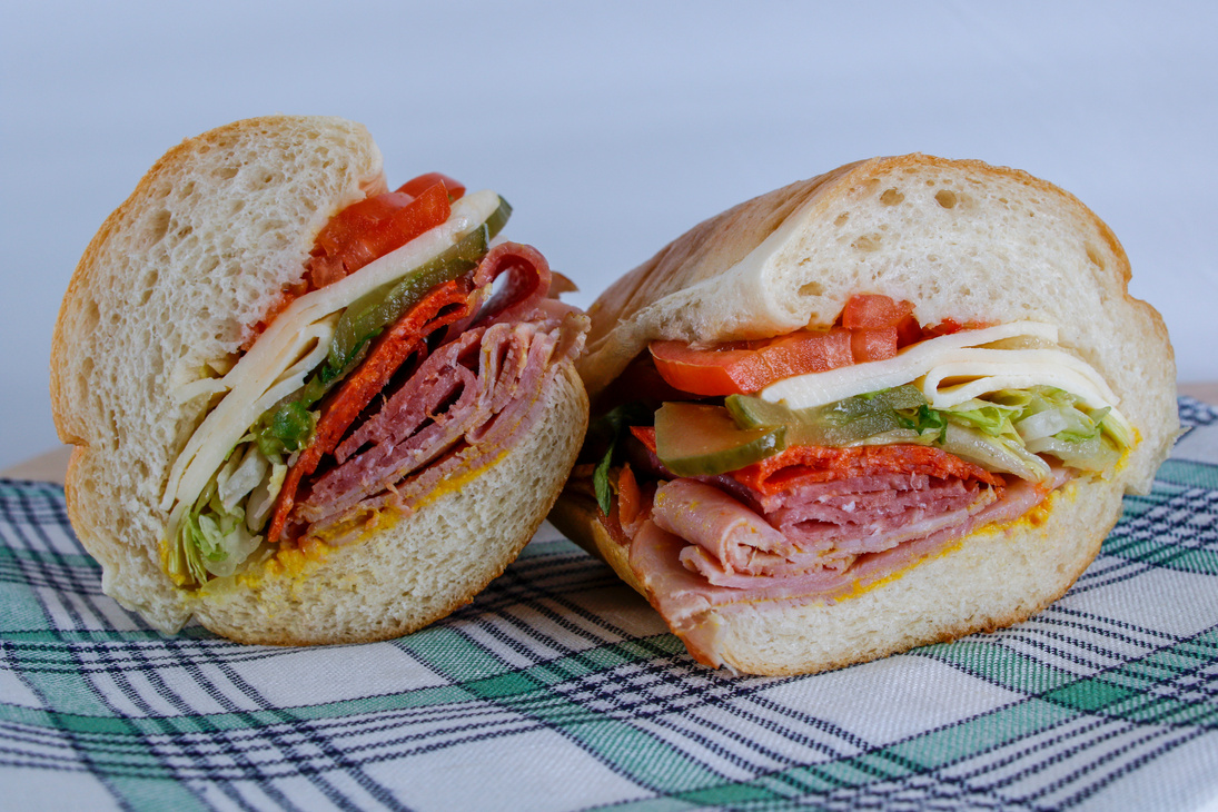 a sandwich with meat, cheese and vegetables on a plaid napkin
